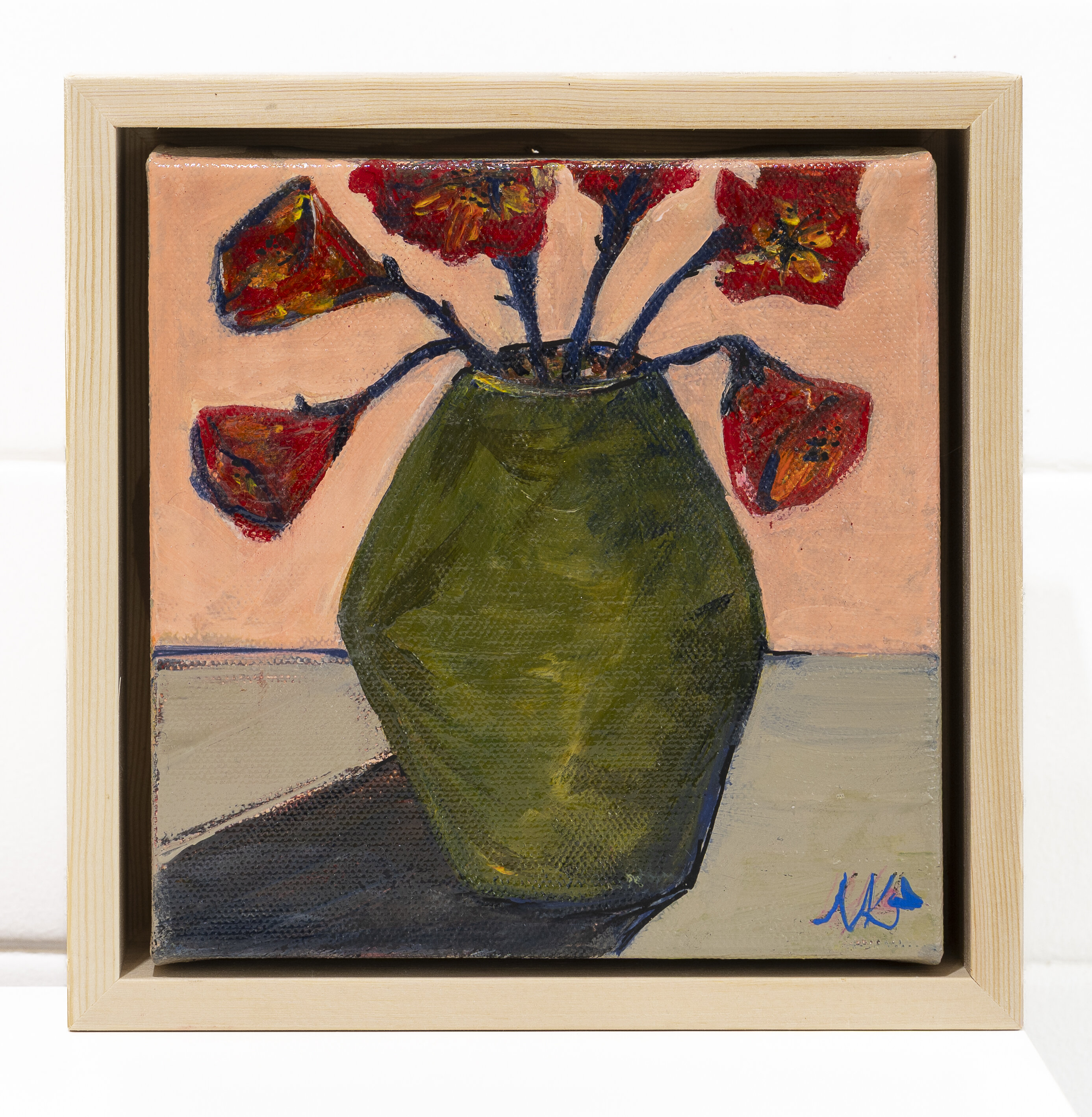 Still life painting of red and orange drooping flowers in a dark olive green vase, against a peach background with a grey-blue table surface.